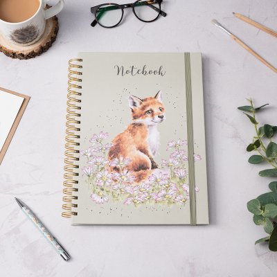 A young fluffy fox exploring a field of daisies on an A4 spiral bound notebook surrounded by stationary on desk