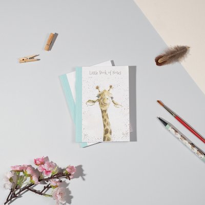 A giraffes head and neck on an A6 paperback notebook surrounded by a pen and paintbrush